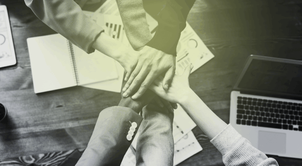 hands coming together in a stack over a table with a computer on it